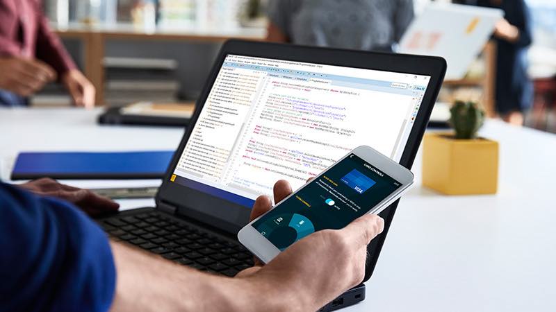 getting-started-800x450 Developer in office environment with open laptop looking at smart phone.